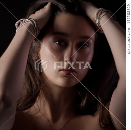 Young woman holding her hair with bracelets and necklace posing in studio Young woman holding her hair with bracelets and necklace posing in studio 132588809