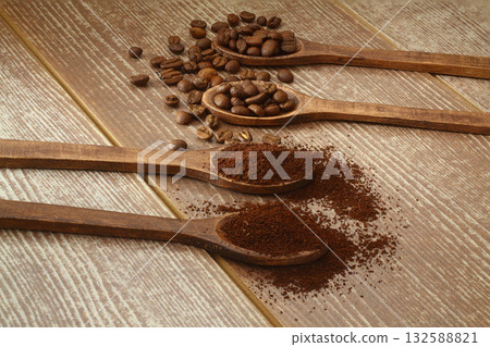 Coffee beans and ground coffee in wooden spoons on brown background. Flat lay. 132588821