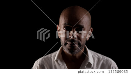 Confident businessman posing in dark room with bright light highlighting his face 132589085