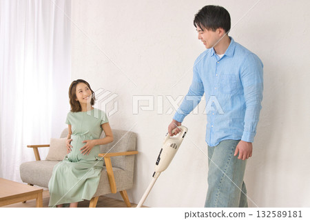 一位年輕男子一邊愉快地吸塵,一邊和孕婦聊天。 一位年輕男子一邊愉快地吸塵,一邊和孕婦聊天。 132589181