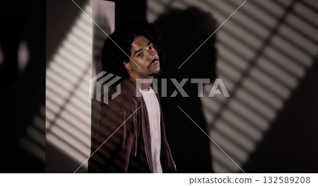 Young african american man posing in a dark room with striped shadows Young african american man posing in a dark room with striped shadows 132589208