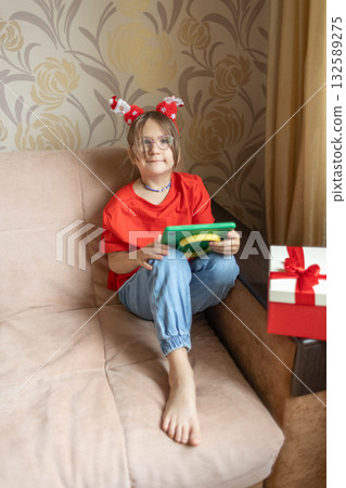 A girl in a Santa Claus hat opens a gift. It's Christmas time. A girl in a Santa Claus hat opens a gift. It's Christmas time. 132589275