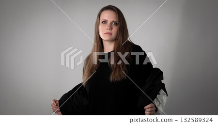 Young woman opening her black jacket on gray background Young woman opening her black jacket on gray background 132589324