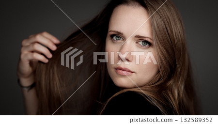 Young woman playing with her long brown hair on gray background Young woman playing with her long brown hair on gray background 132589352