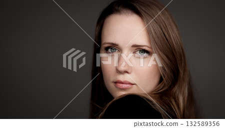 Businesswoman looking over shoulder with serious expression on grey background Businesswoman looking over shoulder with serious expression on grey background 132589356