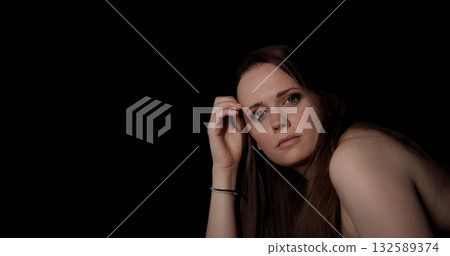 Young woman posing with hand on her head on black background 132589374
