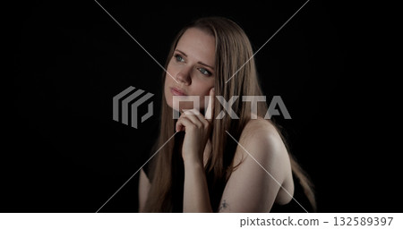 Pensive young woman touching her face and looking away on black background Pensive young woman touching her face and looking away on black background 132589397
