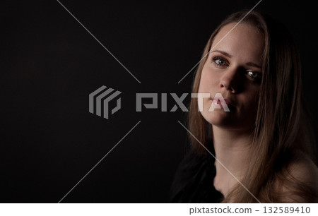 Young woman posing with tilted head and thoughtful expression on black background 132589410