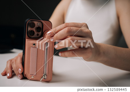 Closeup cropped shot of unrecognizable woman holding sleek smartphone, featuring trendy protective case with hand strap, providing secure hold and contemporary style. Concept of modern technology Closeup cropped shot of unrecognizable woman holding sleek smartphone, featuring trendy protective case with hand strap, providing secure hold and contemporary style. Concept of modern technology 132589445