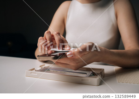 Female professional wiping smartphone screen with sanitizing cloth, eliminating germs and fingerprints during personal device maintenance. Concept of mobile phone maintenance and service. Female professional wiping smartphone screen with sanitizing cloth, eliminating germs and fingerprints during personal device maintenance. Concept of mobile phone maintenance and service. 132589449