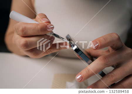 Close-up cropped shot of woman cleaning microphone of smartphone with specialized brush tool, focusing on maintaining optimal audio quality and ensuring hygiene for better communication. Close-up cropped shot of woman cleaning microphone of smartphone with specialized brush tool, focusing on maintaining optimal audio quality and ensuring hygiene for better communication. 132589458