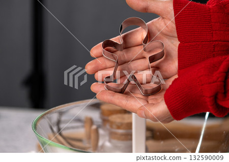 Close-up of hands holding a metal gingerbread man cookie cutter. Christmas baking preparation concept. Festive mood, home cooking, holiday traditions 132590009