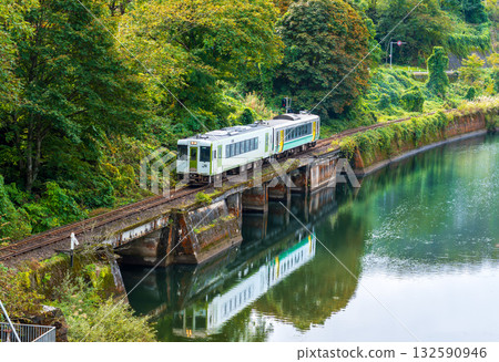 Autumn leaves blooming in the mountains and a locomotive reflected in the Tadami River Autumn leaves blooming in the mountains and a locomotive reflected in the Tadami River 132590946