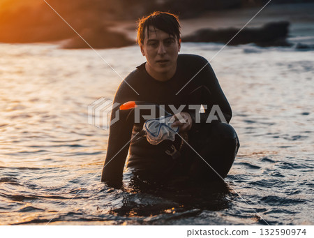 A man is preparing for diving in the ocean at sunset. 132590974