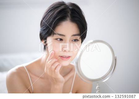 Close-up of a woman looking in the mirror and worrying about skin care problems Close-up of a woman looking in the mirror and worrying about skin care problems 132591087