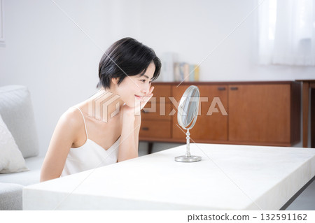 一位留著黑色短髮的美麗女子正在房間的鏡子前檢查自己的護膚情況。美麗,美麗,美麗的肌膚 一位留著黑色短髮的美麗女子正在房間的鏡子前檢查自己的護膚情況。美麗,美麗,美麗的肌膚 132591162