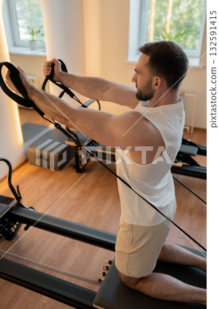 Kneeling pulley exercise, practicing on reformer pulley row focusing on shoulder control Kneeling pulley exercise, practicing on reformer pulley row focusing on shoulder control 132591415