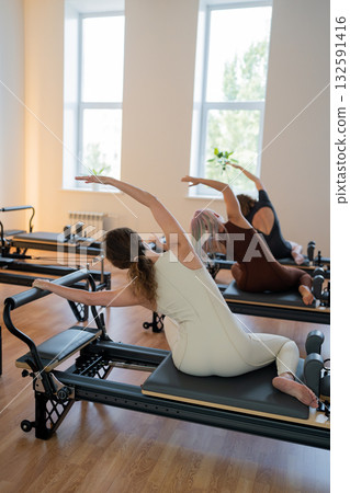 Pilates group of Women doing mermaid exercise in a sunlite modern studio, embodying calm, focus, and strength. Pilates group of Women doing mermaid exercise in a sunlite modern studio, embodying calm, focus, and strength. 132591416