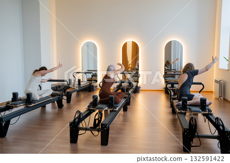 Pilates group of Women doing mermaid exercise in a sunlite modern studio, embodying calm, focus, and strength. 132591422