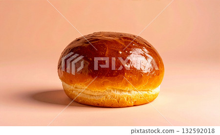 A single, golden-brown brioche bun on a minimal peach-colored background with copy space. A single, golden-brown brioche bun on a minimal peach-colored background with copy space. 132592018