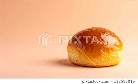 A single, golden-brown brioche bun on a minimal peach-colored background with copy space. 132592019