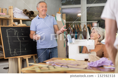 Sewing school senior man teacher conducts lesson for elderly students, draws pattern on black-board Sewing school senior man teacher conducts lesson for elderly students, draws pattern on black-board 132592318