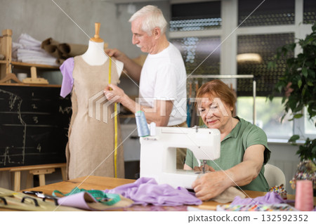 Elderly woman stitching fabric on machine in sewing class for seniors Elderly woman stitching fabric on machine in sewing class for seniors 132592352