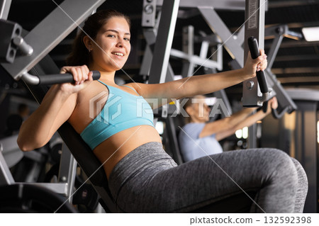 Sporty young girl exercising on chest press machine in gym 132592398