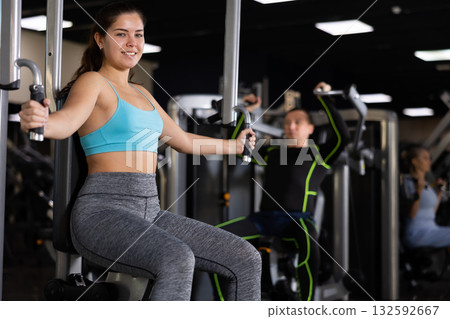 Girl performing butterfly exercise for chest in pec deck machine 132592667
