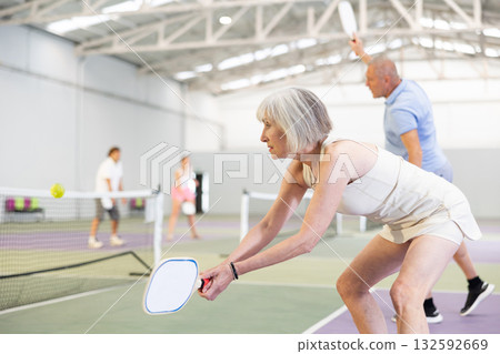 Positive elderly woman playing pickleball on indoor court Positive elderly woman playing pickleball on indoor court 132592669
