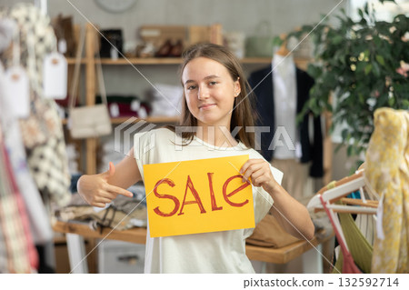 Young teenage girl holding a sign saying Sale in the interior of fashion store Young teenage girl holding a sign saying Sale in the interior of fashion store 132592714