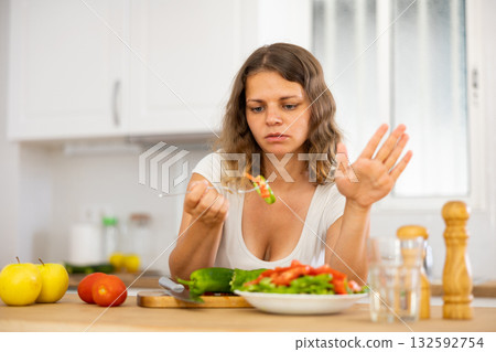 Sad woman eating vegetable salad in kitchen 132592754