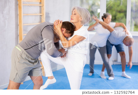 Senior woman in pair with middle-aged coach train Krav Maga and self-defense skills. 132592764