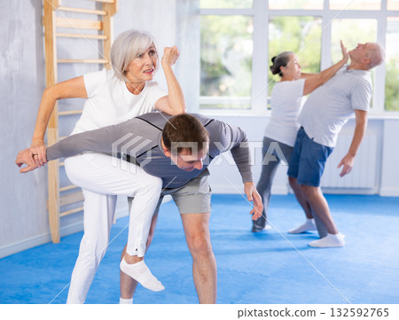 Senior woman in pair with middle-aged coach train Krav Maga and self-defense skills. 132592765
