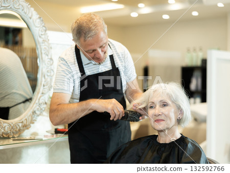 Professional male hairdresser cuts hair of elderly woman at beauty salon 132592766