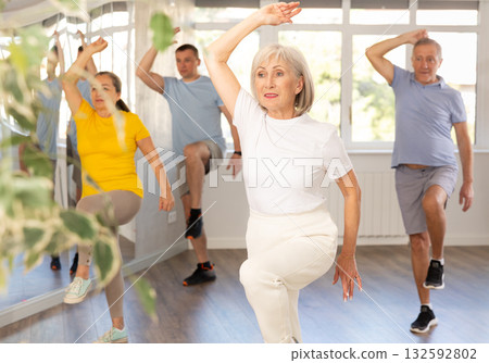 Cheerful elderly woman learning dynamic dances at group choreography lesson Cheerful elderly woman learning dynamic dances at group choreography lesson 132592802