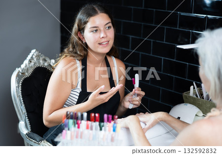 Skilled woman manicurist filing and shaping nails of female client during procedure of manicure in beauty salon 132592832