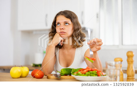 Sad woman eating vegetable salad in kitchen 132592839