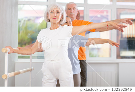 Active mature woman practicing second position holding by ballet barre together with others 132592849