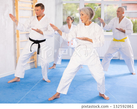Old woman attendee of karate classes practicing kata standing in row with others 132592861
