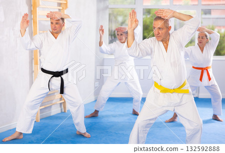 Old man attendee of karate classes practicing kata standing in row with others 132592888