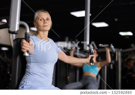 Focused mature female athlete using chest fly machine in gym Focused mature female athlete using chest fly machine in gym 132592893