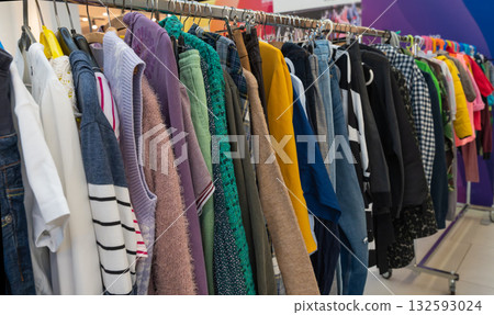 Various clothes hanging on racks at an eco swap event. Sweaters, shirts, and jeans in different colors and textures symbolize reuse, sustainability, and eco-friendly fashion choices. 132593024