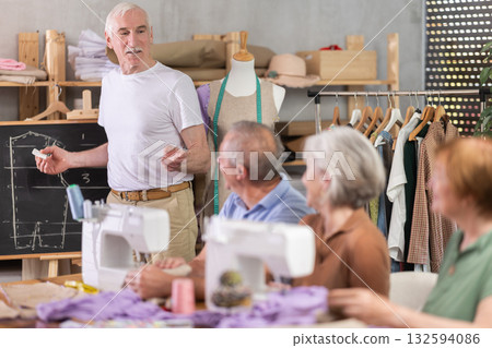 Aged teacher explaining pattern structure by chalkboard during sewing course for seniors 132594086