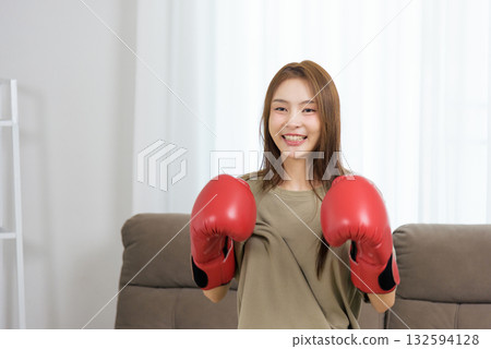 Young happy woman home activity, confident person wearing red boxing gloves, smiling with bright energetic mood, ready for fitness training session 132594128