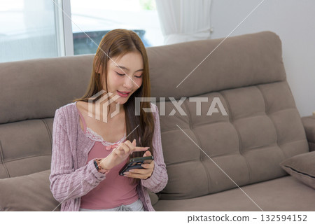 Young woman happy home activity, people enjoy mobile phone interaction, browsing social media, chatting friends, enjoying casual leisure time on cozy couch, feeling contentment Young woman happy home activity, people enjoy mobile phone interaction, browsing social media, chatting friends, enjoying casual leisure time on cozy couch, feeling contentment 132594152