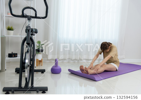Young woman enjoys home activity, stretching on yoga mat fitness equipment nearby promoting happy healthy active people living daily exercise 132594156