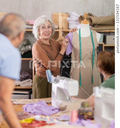 Elderly female teacher showing how to sew on mannequin 132594167