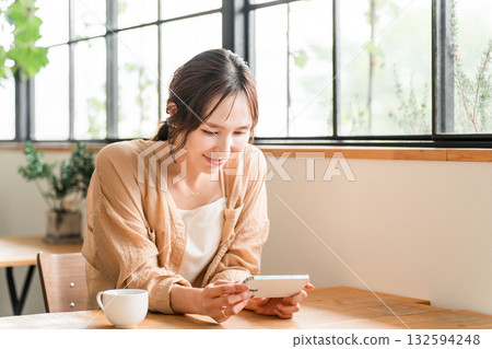 Young Asian woman drinking coffee in the living room of a cafe and looking at her smartphone Young Asian woman drinking coffee in the living room of a cafe and looking at her smartphone 132594248