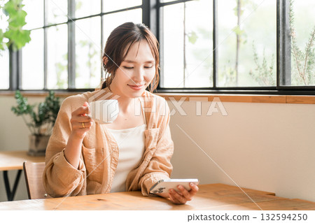 Young Asian woman drinking coffee in the living room of a cafe and looking at her smartphone 132594250